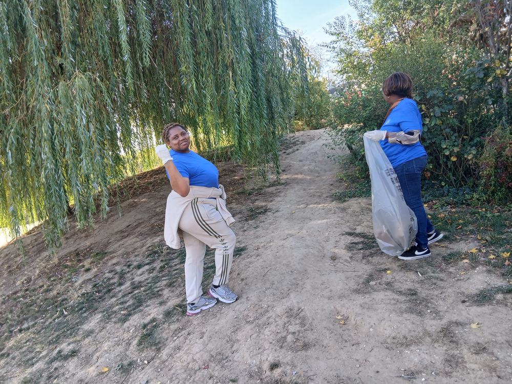 Two volunteers collecting litter along a path under a willow tree